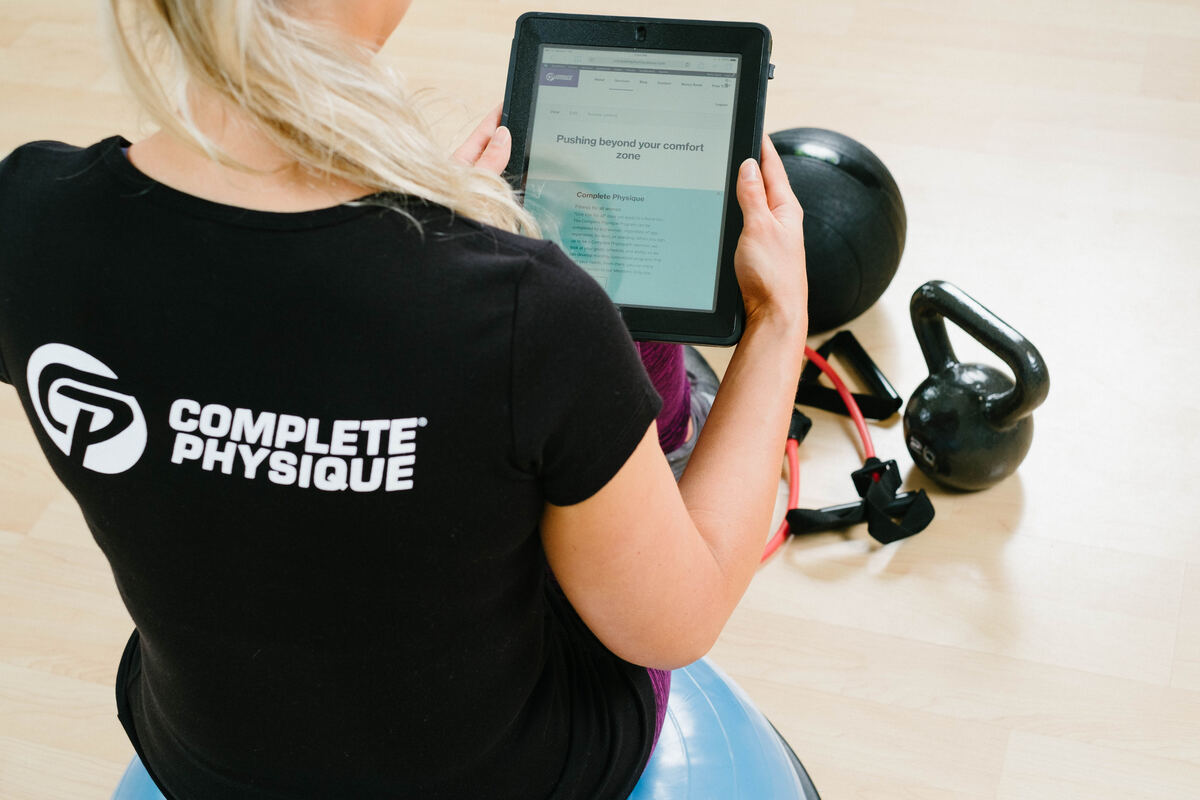 A coach in a Complete Physique shirt reviewing a client program on a tablet
